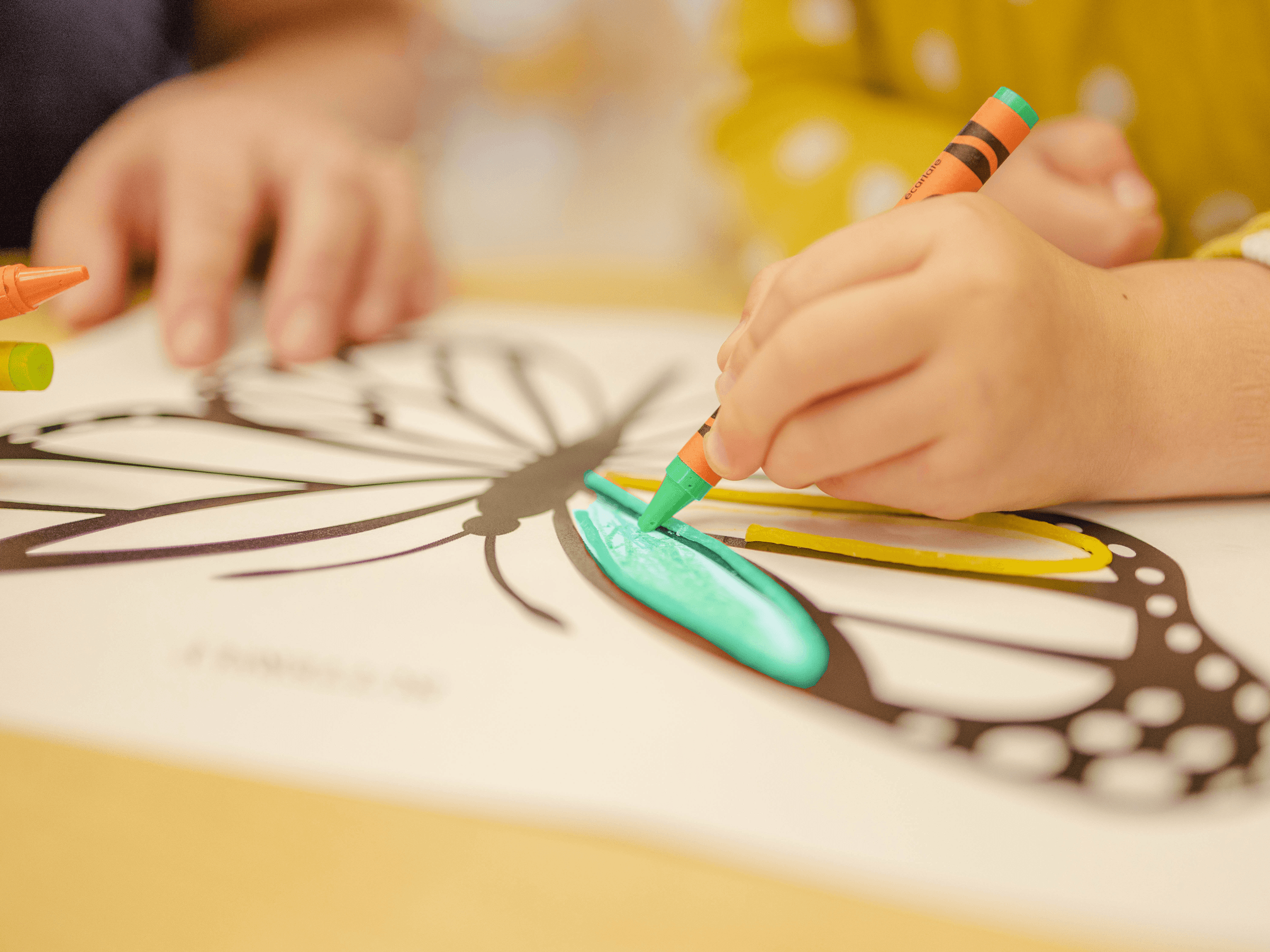 Kind malt Schmetterling mit grünem Wachsmalstift auf Papier.