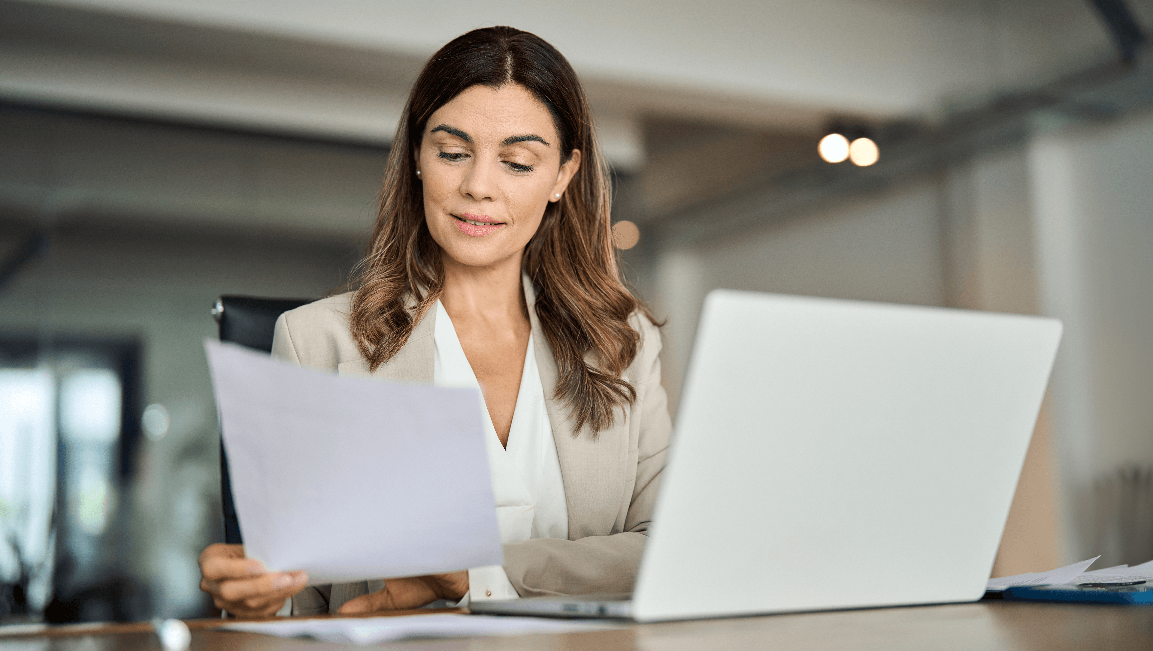 Headerbild zeigt eine Frau, die vor dem Laptop sitzt und ein Blatt Papier liest, um in ihrem KMU die Digitalisierung mit askDANTE voranzutreiben.