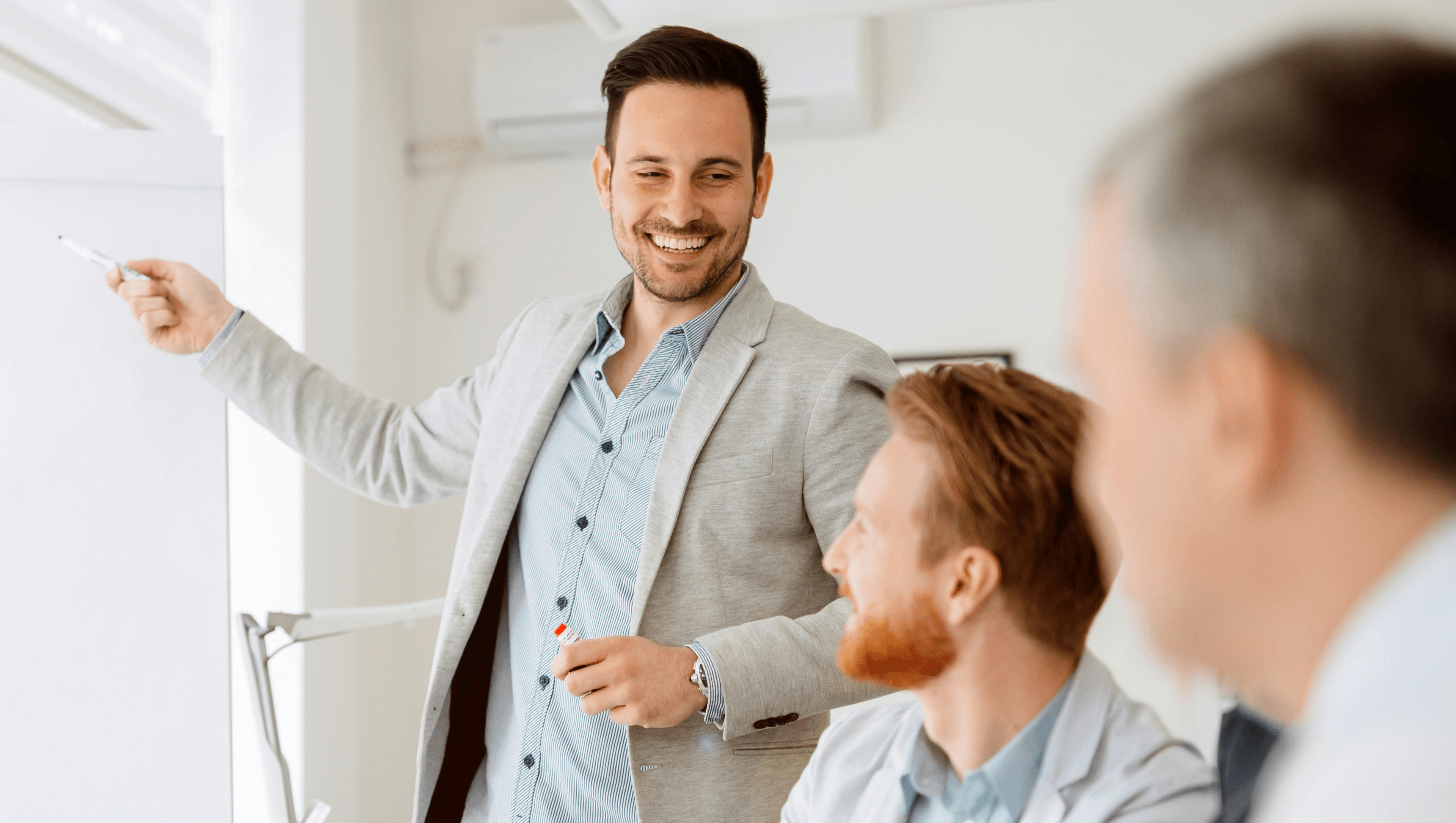 Headerbild zeigt lachenden Mann, der im Personalmanagement arbeitet und seinen Kollegen mit einem Stift die Vorteile von askDANTE an einem Flipchart zeigt.